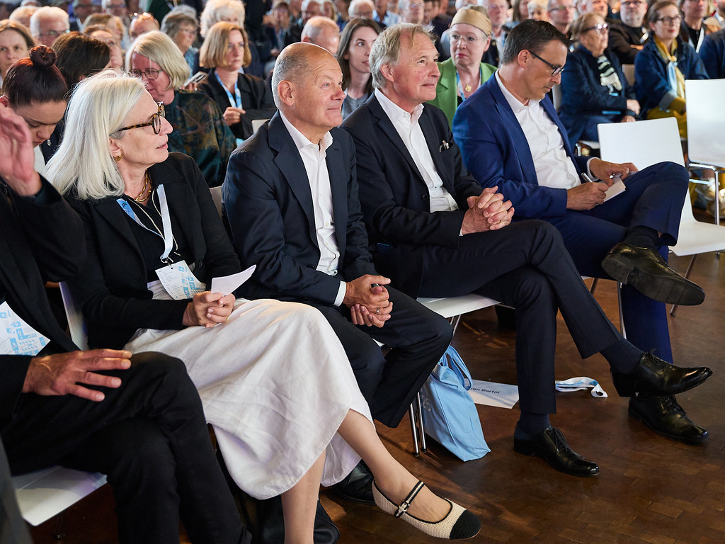 Ein Publikum, darunter Olaf Scholz, hört auf einer Veranstaltung aufmerksam zu.