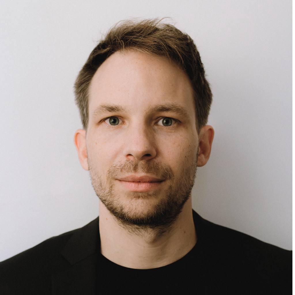 **Porträt eines Mannes mit kurzem Haar vor heller Wand, schwarzes Hemd.**