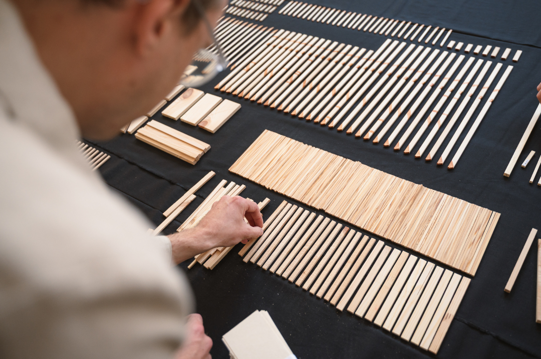 Benedikt Stöhrer Person ordnet nach Größe sortierte Holzstäbchen auf schwarzem Tuch an.