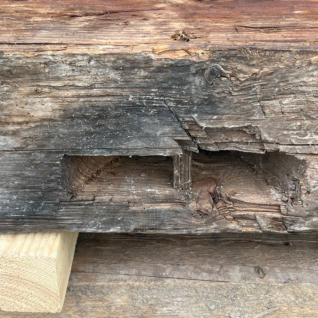 Alt-Text: Abgenutztes Holzbalken mit Rissen und Schnitteinschnitten, sichtbare Holzfasern und eine Einlassung; minimaler Aufbau aus Holzkonstruktion.