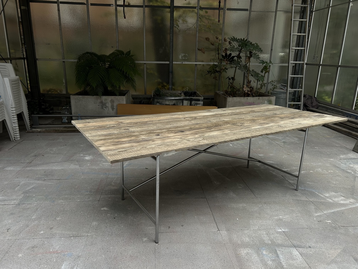 Rechteckiger Tisch mit rustikaler Holzplatte und schlichtem Metallgestell in einem Wintergarten.